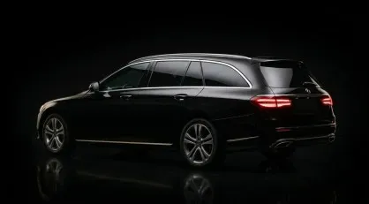 Un'inquadratura professionale e low-key di tre quarti posteriore di una Mercedes Classe E Station Wagon nera lucida, illuminata da luci di profilo su sfondo nero assoluto.