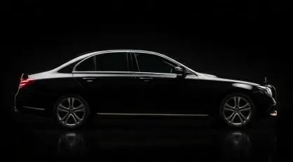 Un profilo laterale professionale e low-key di una Mercedes Classe E berlina nera lucida, illuminata da luci di profilo su sfondo nero assoluto, in formato 418x231px, per la sezione flotta.